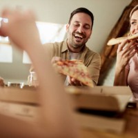 happy couple eating pizza for lunch at home. - junk food stock pictures, royalty-free photos & images