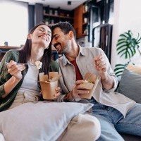 happy couple laughing and eating takeaway food at home - junk food stock pictures, royalty-free photos & images