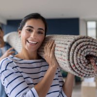 happy couple moving house and carrying a rolled up carpet - home decoration stock pictures, royalty-free photos & images