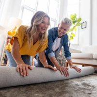 happy couple moving house and unrolling a carpet while unpacking - home decoration stock pictures, royalty-free photos & images
