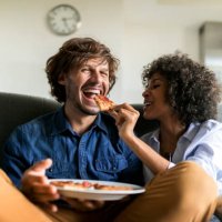 happy couple sitting on couch eating pizza - junk food stock pictures, royalty-free photos & images