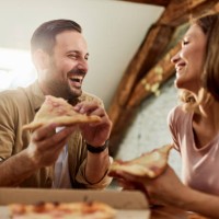 happy couple talking while eating pizza for lunch at home. - junk food stock pictures, royalty-free photos & images