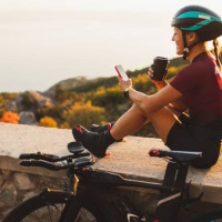happy cyclist woman relaxing after long ride, drinking coffee, smiling and chatting in mobile smartphone at sunset - junk food stock pictures, royalty-free photos & images