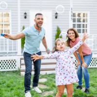 happy family playing soap bubbles on the grass in front of their porch. adorable little girl playing soap bubbles with her mother and father outdoors. - garden decoration stock pictures, royalty-free photos & images