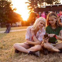happy female festival goers using mobile phone at sunset. - concert stock pictures, royalty-free photos & images
