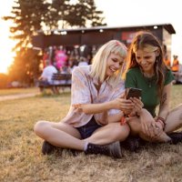 happy female festival goers using smart phone at sunset. - concert stock pictures, royalty-free photos & images