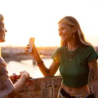 happy female friends using mobile phone at sunset. - concert stock pictures, royalty-free photos & images