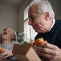 happy grandfather and grandson eating burger together at home - junk food stock pictures, royalty-free photos & images