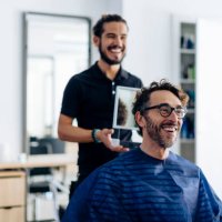 happy hairdresser showing haircut to client in mirror at salon - hairstyle photos et images de collection