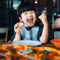 happy little asian girl enjoying pizza lunch in an outdoor restaurant, with a giant pizza in front of her on the dining table. looking at camera and smiling joyfully. eating out lifestyle - food stock pictures, royalty-free p