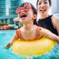 happy little asian girl with sunglasses smiling joyfully and enjoying family bonding time with mother, having fun in the swimming pool on summer vacations - travel stock pictures, royalty-free photos & images