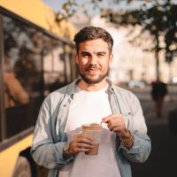 happy man holding cup of coffee while standing on street during summer - junk food stock pictures, royalty-free photos & images