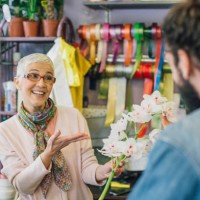 happy senior florist showing a flower to a customer - garden decoration stock pictures, royalty-free photos & images