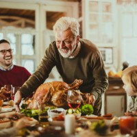 happy senior man serving thanksgiving turkey for his family at dining table. - home decoration stock pictures, royalty-free photos & images