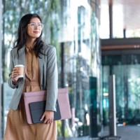 happy successful asian businesswoman holding a takeaway coffee cup and files on the street next to a glass building - junk food stock pictures, royalty-free photos & images