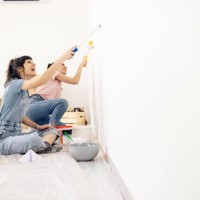 happy twin sisters painting walls while moving into their new apartment - home decoration stock pictures, royalty-free photos & images