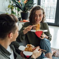 happy woman and man with take out food talking in living room at home - junk food stock pictures, royalty-free photos & images