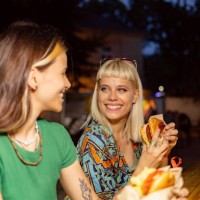 happy woman eating and talking to her friend on a music festival by night. - junk food stock pictures, royalty-free photos & images