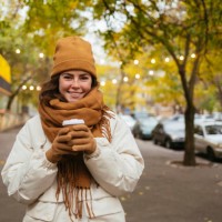 happy woman holding disposable coffee cup on sidewalk during autumn - junk food stock pictures, royalty-free photos & images