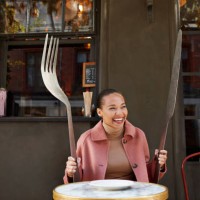 happy woman holding large fork and table knife while sitting at sidewalk cafe - food stock pictures, royalty-free photos & images