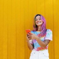 happy woman holding mobile phone in front of yellow wall - fashion stock pictures, royalty-free photos & images