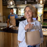 happy woman leaving a cafe carrying a bag of pastries - junk food stock pictures, royalty-free photos & images