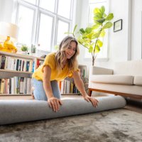 happy woman moving house and unrolling a carpet while unpacking - home decoration stock pictures, royalty-free photos & images