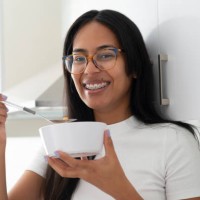 happy woman, portrait and eating porridge in bowl for morning, breakfast or meal in kitchen at home. face of female person smile with glasses for delicious snack, fiber or calcium vitamins at house - food stock pictures, roya