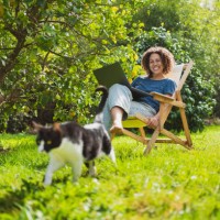 happy woman with laptop looking at cat while sitting on deck chair by lemon tree - garden decoration photos et images de collection