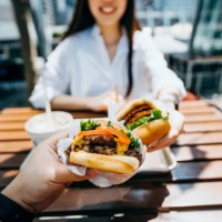 happy young asian couple eating beef burger with fries in an outdoor fast food restaurant - junk food stock pictures, royalty-free photos & images