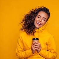 happy young cheerful girl laughing and holding cup of coffee on colored yellow background - fashion stock pictures, royalty-free photos & images