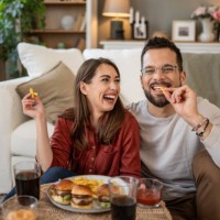 happy young couple eating fast food at home and watching movie on tv - junk food stock pictures, royalty-free photos & images