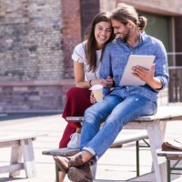 happy young couple sitting on table in a beer garden with tablet - junk food stock pictures, royalty-free photos & images