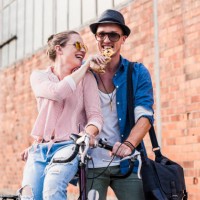 happy young couple with bicycle sharing a snack - fashion stock pictures, royalty-free photos & images