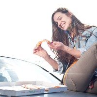happy young woman eating pizza on car hood - junk food stock pictures, royalty-free photos & images