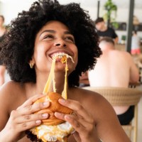 happy young woman enjoying a delicious burger at a restaurant during summer vacation - junk food stock pictures, royalty-free photos & images