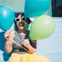 happy young woman holding balloons while sitting on bench - fashion photos et images de collection