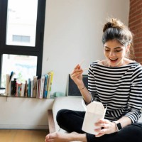 happy young woman sitting on couch at home having asian takeaway food - junk food stock pictures, royalty-free photos & images