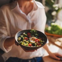 healthy dinner or lunch. woman in t-shirt and jeans standing and holding vegan superbowl or buddha bowl with hummus, vegetable, salad, beans, couscous and avocado and smoothie in hands, square crop - food stock pictures, roya