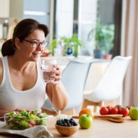 healthy eating concept. woman drinkig water while having a healthy meal of salad and fruits - food stock pictures, royalty-free photos & images