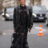 Helena Bordon wears silver earrings, a black leather oversized jacket, a black long lace dress, a black leather bag, black leather shoes, outside...