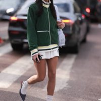Heloise Agostinelli seen wearing a green and white Lacoste tennis skirt, green Lacoste jacket, white socks, grey heels, Lacoste white leather bag...