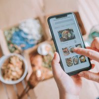 high angle view close up asian woman using meal delivery service ordering food online with mobile app on smartphone in the living room at a cozy home - food stock pictures, royalty-free photos & images