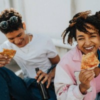 high angle view of curly hair woman eating pizza with male friend while sitting at parking lot - junk food stock pictures, royalty-free photos & images
