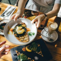 high angle view of woman passing platter of food to friend during brunch in an outdoor restaurant against beautiful sunlight - food fotografías e imágenes de stock