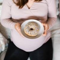 high angle view of young pregnant woman holding a plate of donut, enjoying her cravings. unhealthy diet during pregnancy. food cravings during pregnancy - junk food stock pictures, royalty-free photos & images
