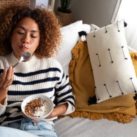 high angle view of young relaxed happy multiracial latina woman eating healthy granola and yogurt breakfast sitting on the couch at home cozy living room. copy space. - food photos et images de collection