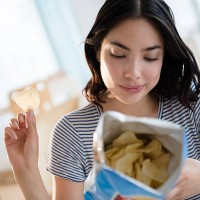 hispanic woman reading ingredients on bag of potato chips - junk food stock pictures, royalty-free photos & images