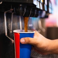 holding a cup at soft drink self service machine pouring cola fizzy drink at a restaurant. - junk food stock pictures, royalty-free photos & images