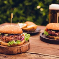 huge gourmet cheese burgers on a rustic wooden table outdoors - food stockfoto's en -beelden